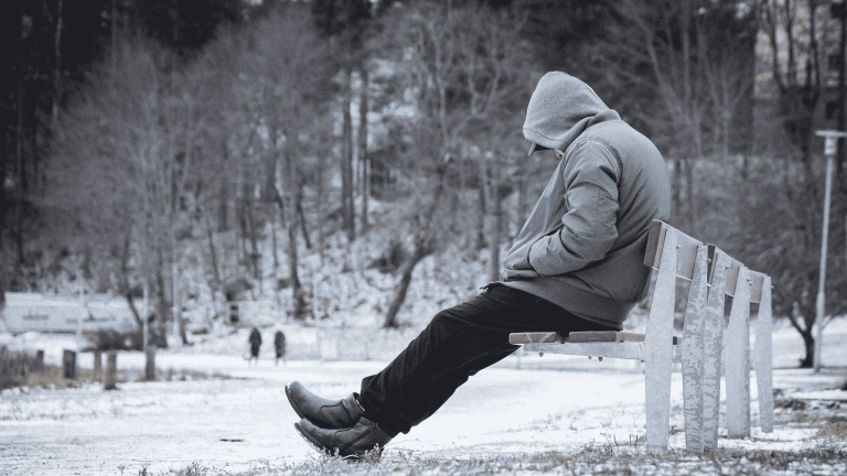 Een man die alleen zit op een bankje in de winter